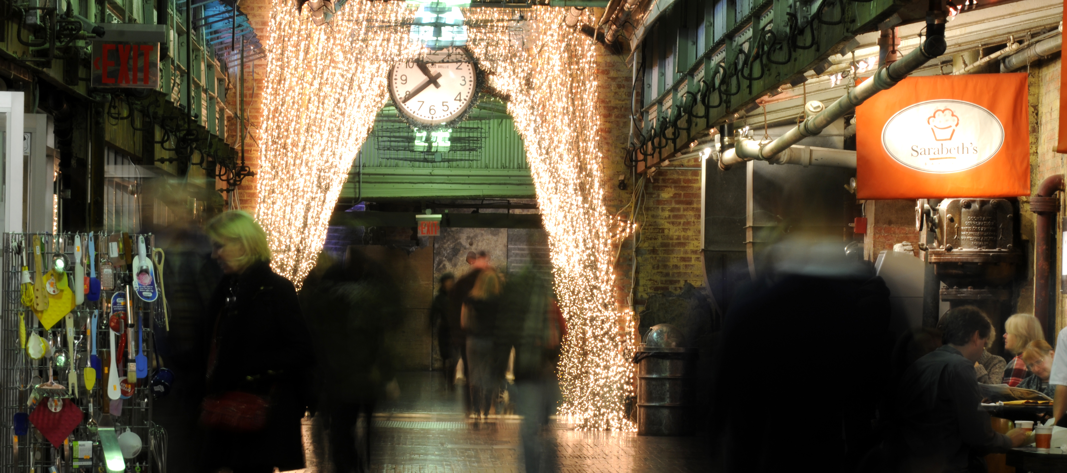 Illuminated entrance to a covered market with shoppers and decorative lighting.