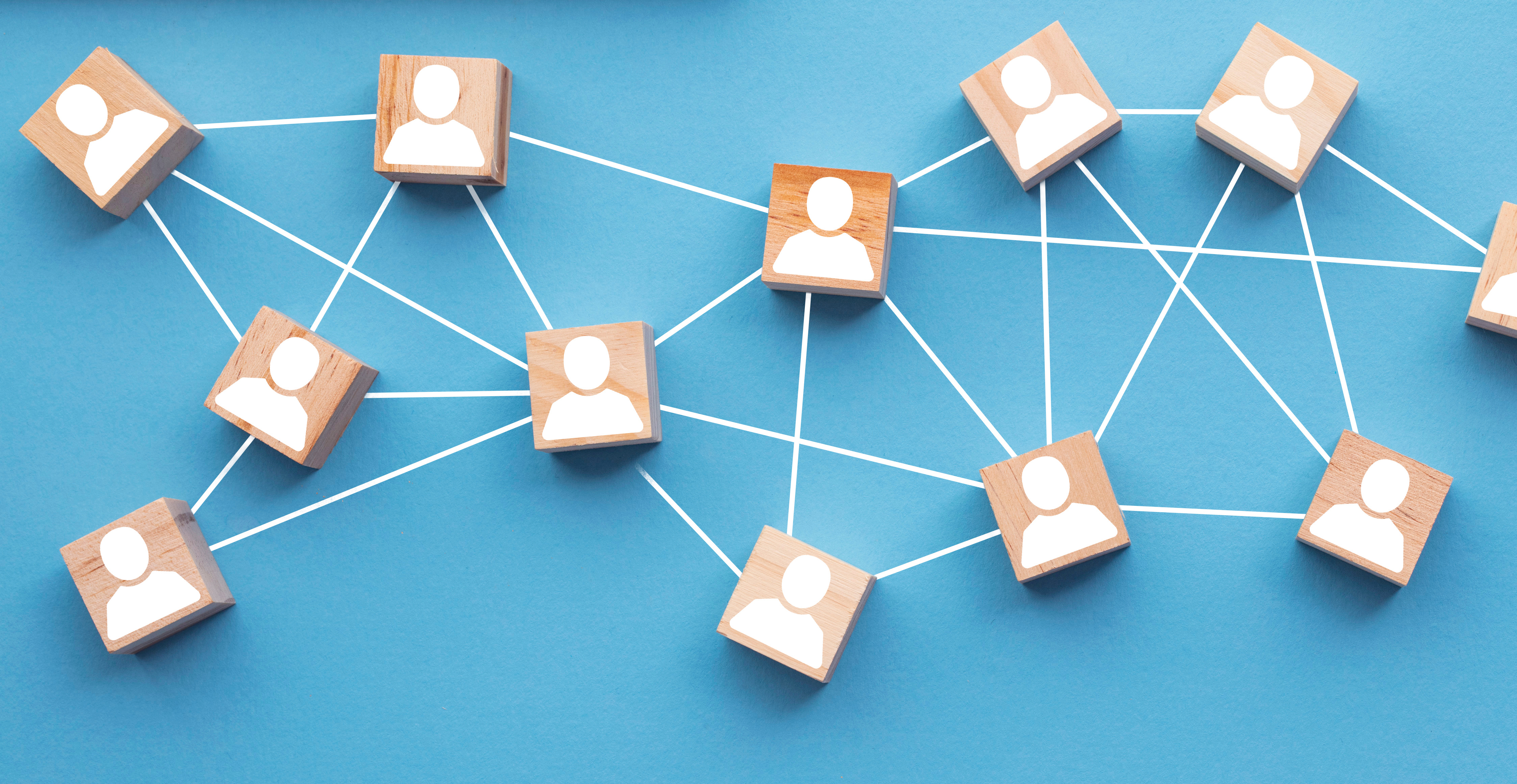 Wooden blocks with person icons connected by white lines on blue surface, representing network connections