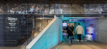 People viewing an illuminated display in a modern building with glass partitions.
