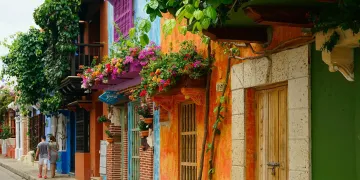 Colorful building facades with bright flowers and greenery in a Mediterranean-style street.
