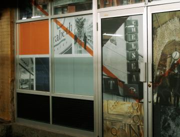 A storefronts with large glass windows, some covered with orange and white panels.