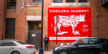 A red billboard showing a cow diagram with meat cuts on a brick building, labeled "Chelsea Market".