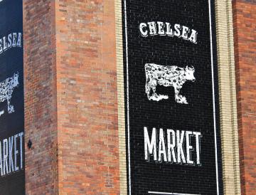 Black sign on brick wall with "CHELSEA MARKET" text and cow illustration.