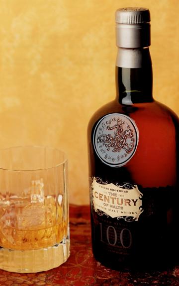 A bottle of aged Bunnahabhain whisky next to a crystal tumbler against a golden backdrop.