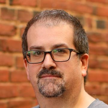 Middle-aged man with glasses and goatee against exposed brick wall