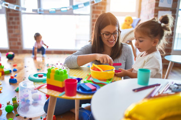 Teacher and young student playing with colorful stacking rings at a bright classroom table