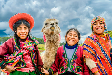 Three people in traditional Peruvian clothing posing with a white llama under cloudy sky